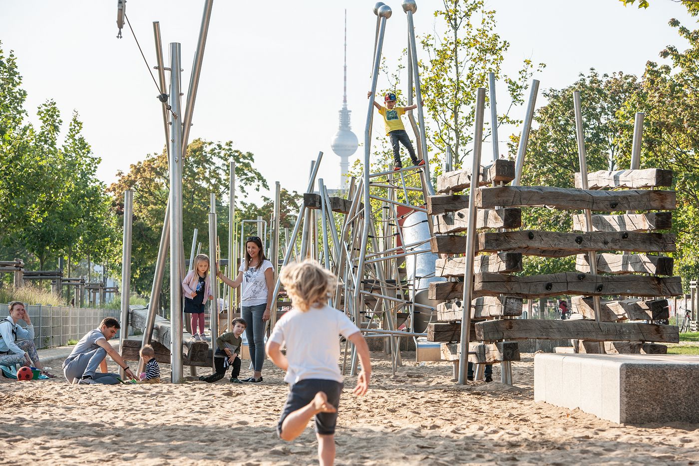 Das Bild zeigt Kinder auf dem Spielplatz im Mauerpark, im Hintergrund ist der Fernsehturm zu sehen.