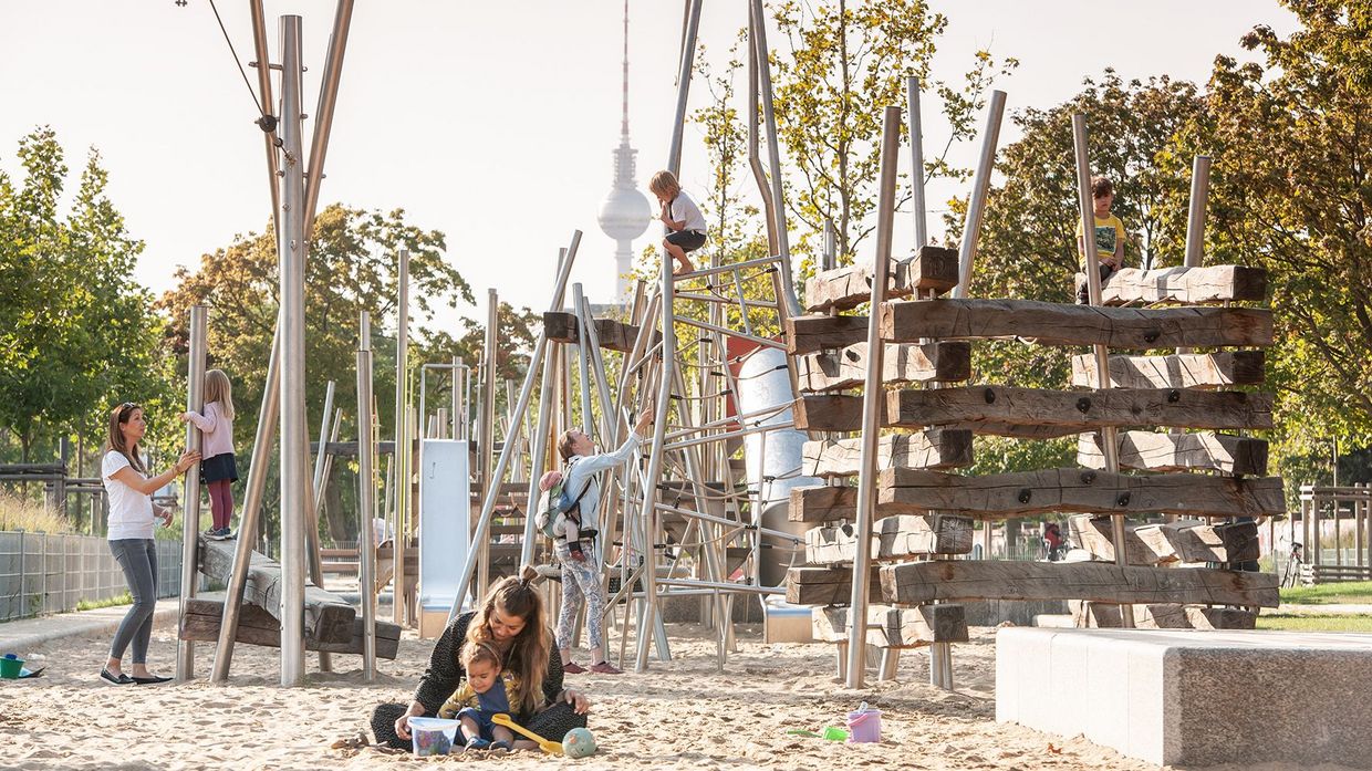 Das Bild zeigt Kinder, die auf dem Spielplatz spielen. Im Hintergrund ist der Fernsehturm zu erkennen.