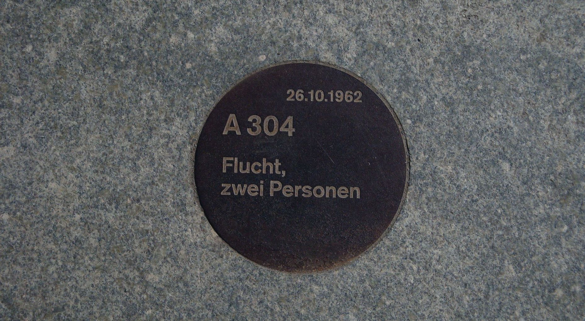 Das Bild zeigt eine runde in Stein eingelassene Tafel auf dieser steht: 26.10.1961, A 304, Flucht, zwei Personen