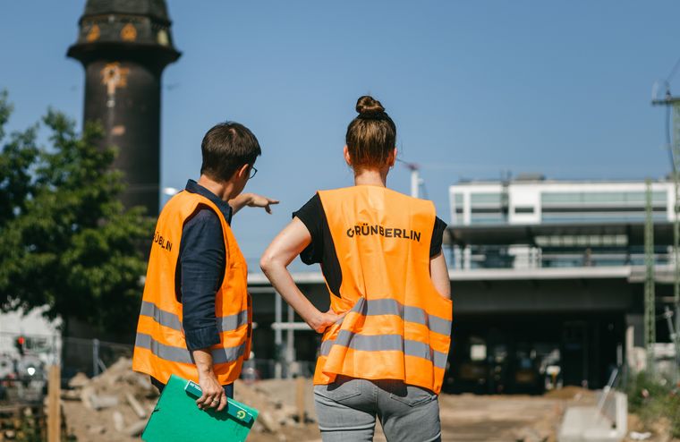 Zwei Projektleiterinnen von Grün Berlin stehen in orangenen Warnwesten auf einer Baustelle am Bahnhof Ostkreuz