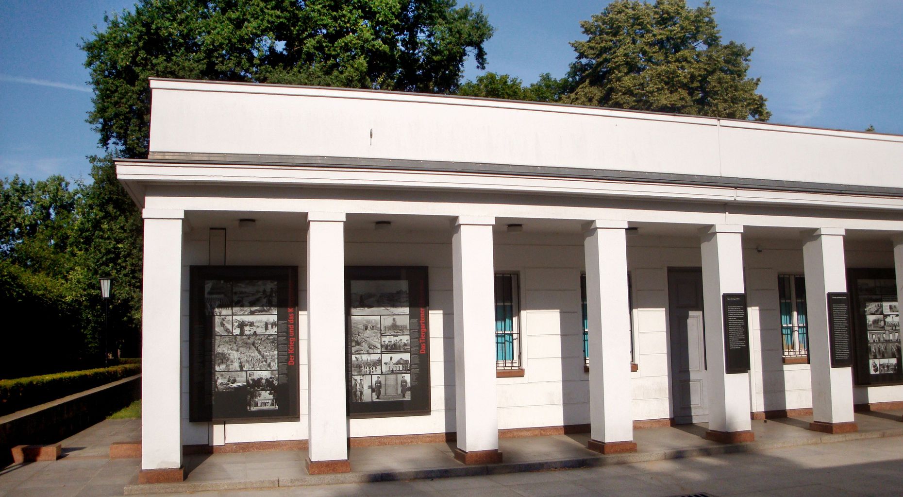 Das Bild zeigt ein weißes Gebäude. Es wird als Galerie genutzt, es sind Informationstafeln zu sehen.
