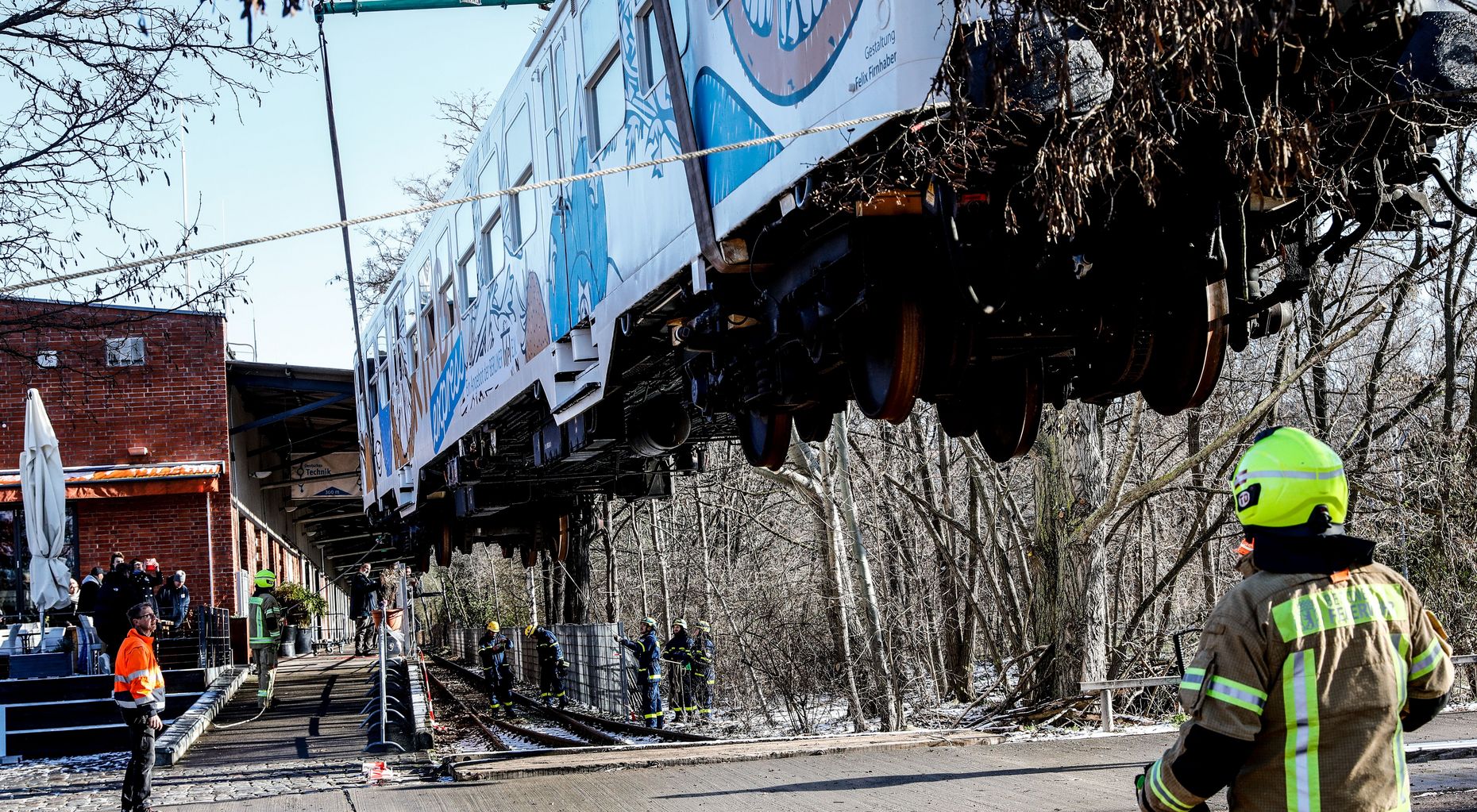 Ein ausrangierter weißer Bahnwaggon wird von einem Kran über Bäume hinweg gehoben.