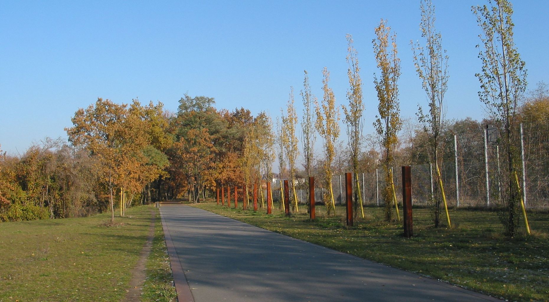 Das Bild zeigt einen Weg im Hans Baluschek Park, an den Seiten stehen rostrote Metallstreben aus dem Boden.