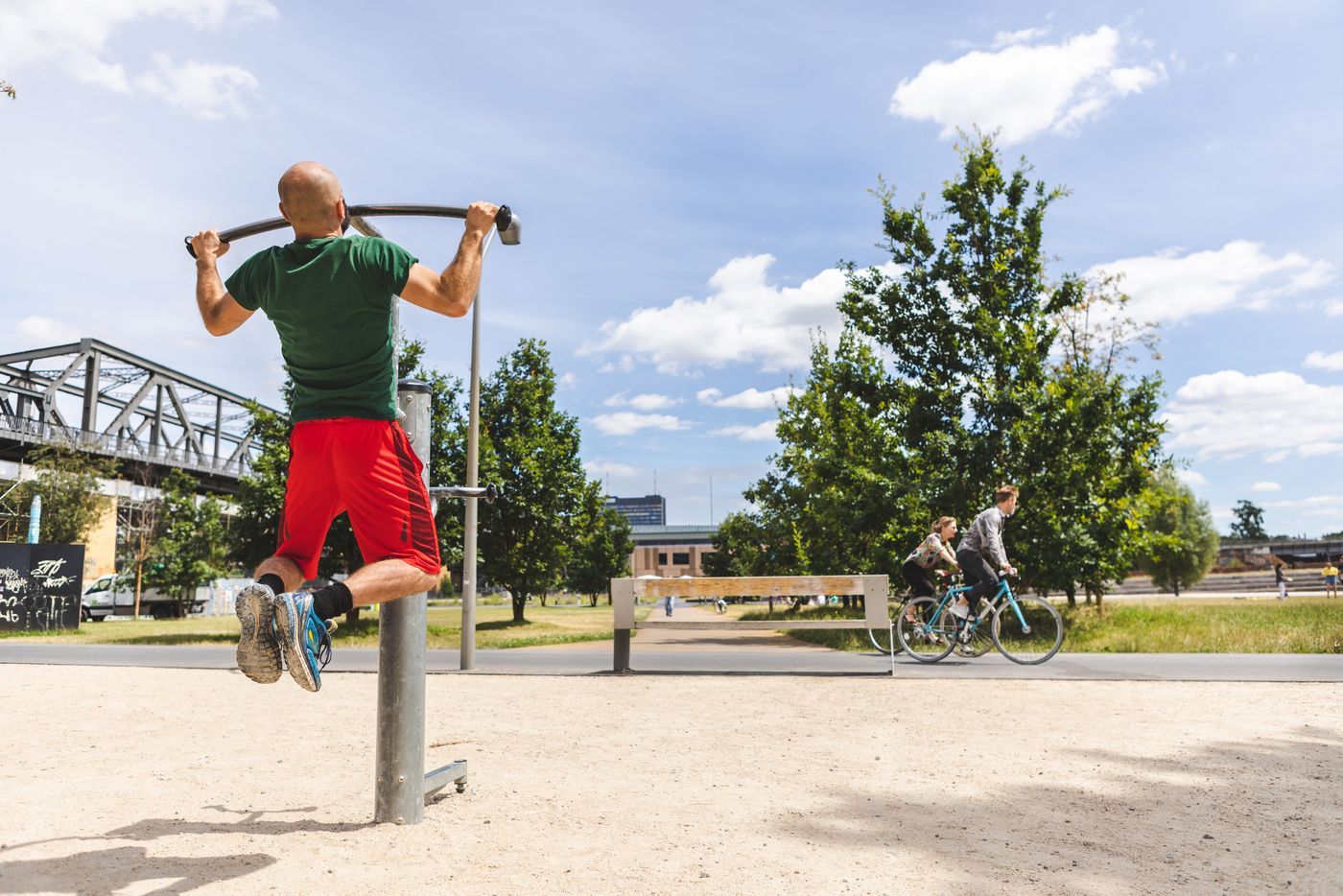 Eine Mann an den Sportgeräten im Gleisdreieck Park, im Hintergrund radeln zwei Personen.