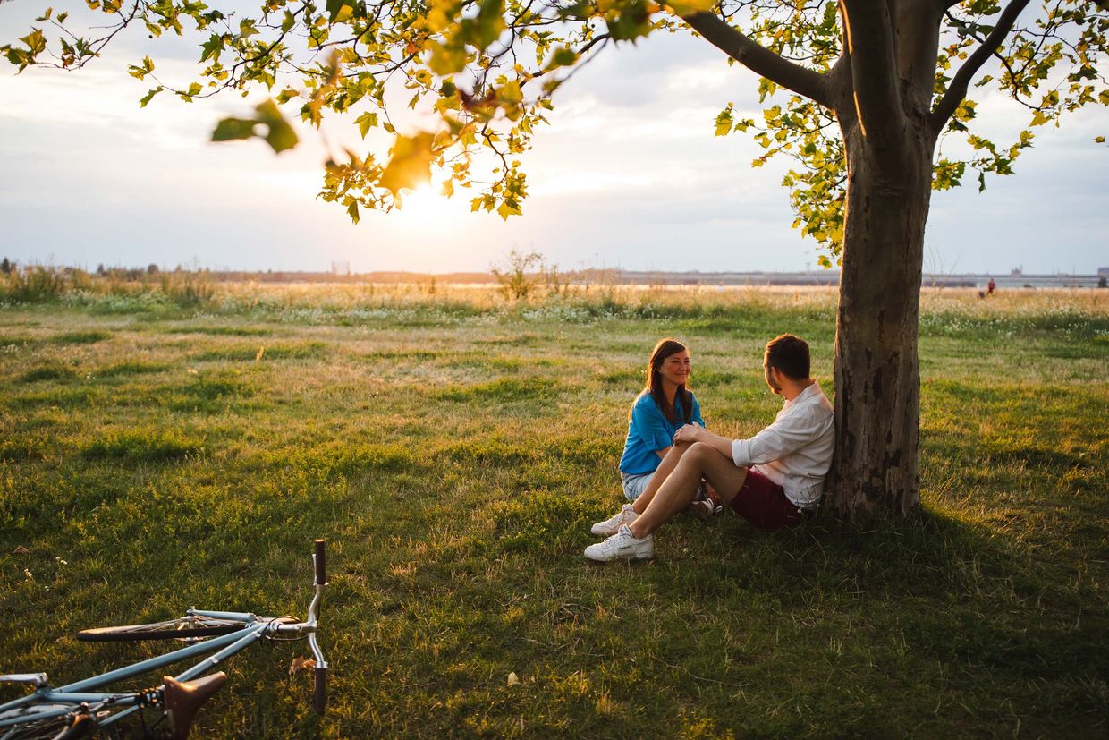Eine Frau und ein Mann sitzen an einem Baum auf dem Tempelhofer Feld.