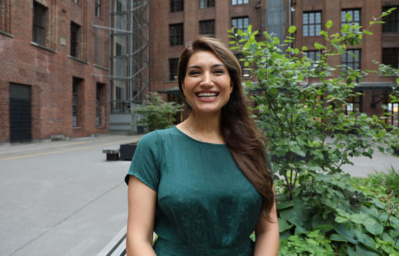 Foto von Finanzbuchhalterin Bahareh Shahmoradi in einem dunkelgrünen Kleid vor grünen Sträuchern im Innenhof des Ullsteinhauses