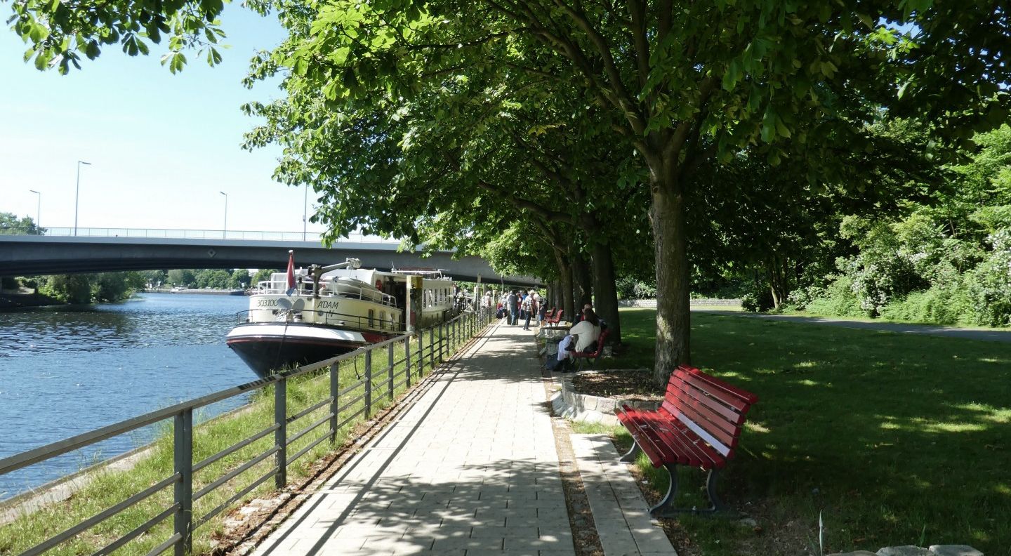 Das Schiffahrtsufer des Havel Radwegs, Leute sitzen am Rand auf roten Bänken.