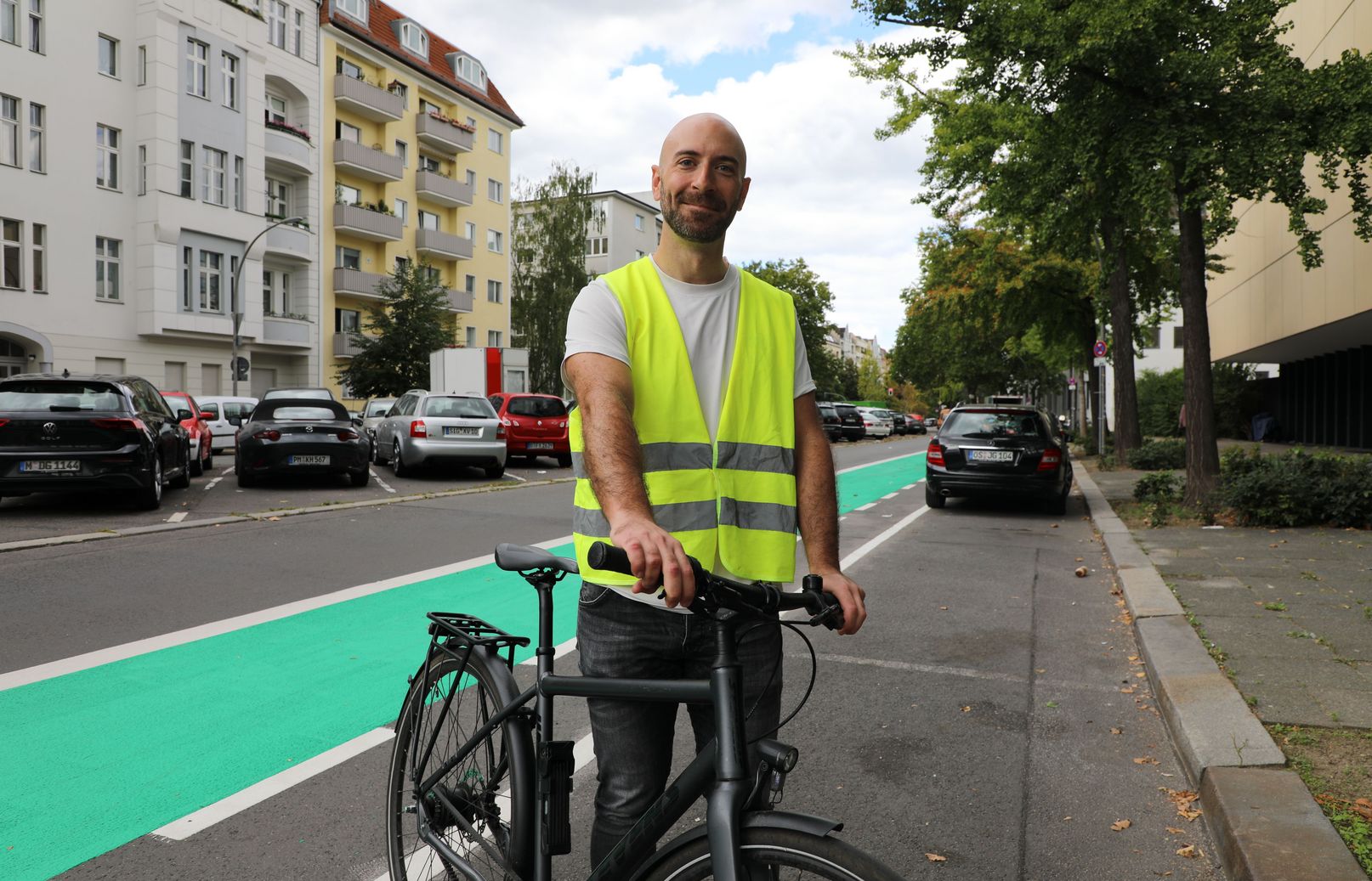 Nikolaos Rousiamanis, Projektmanager bei infraVelo, steht mit einer neongelben Warnweste und seinem Fahrrad vor einer neuen leuchtend grün markierten Fahrradspur