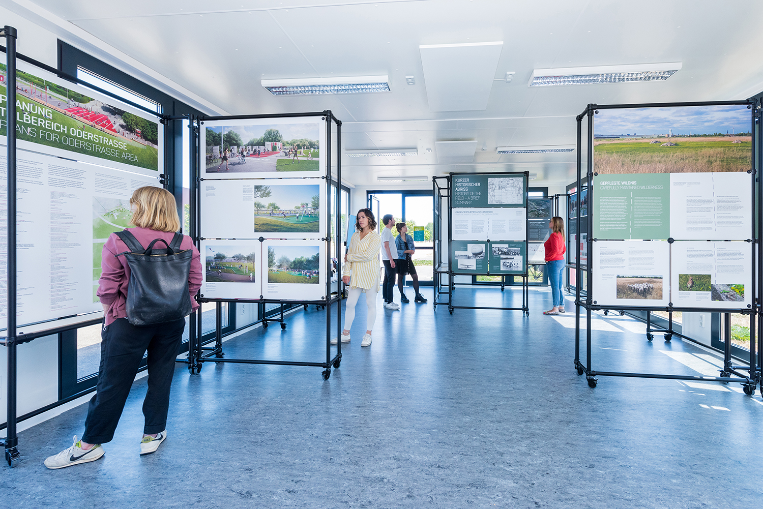 Menschen stehen im Infopavillon auf dem Tempelhofer Feld und schauen sich Ausstellungstafeln an